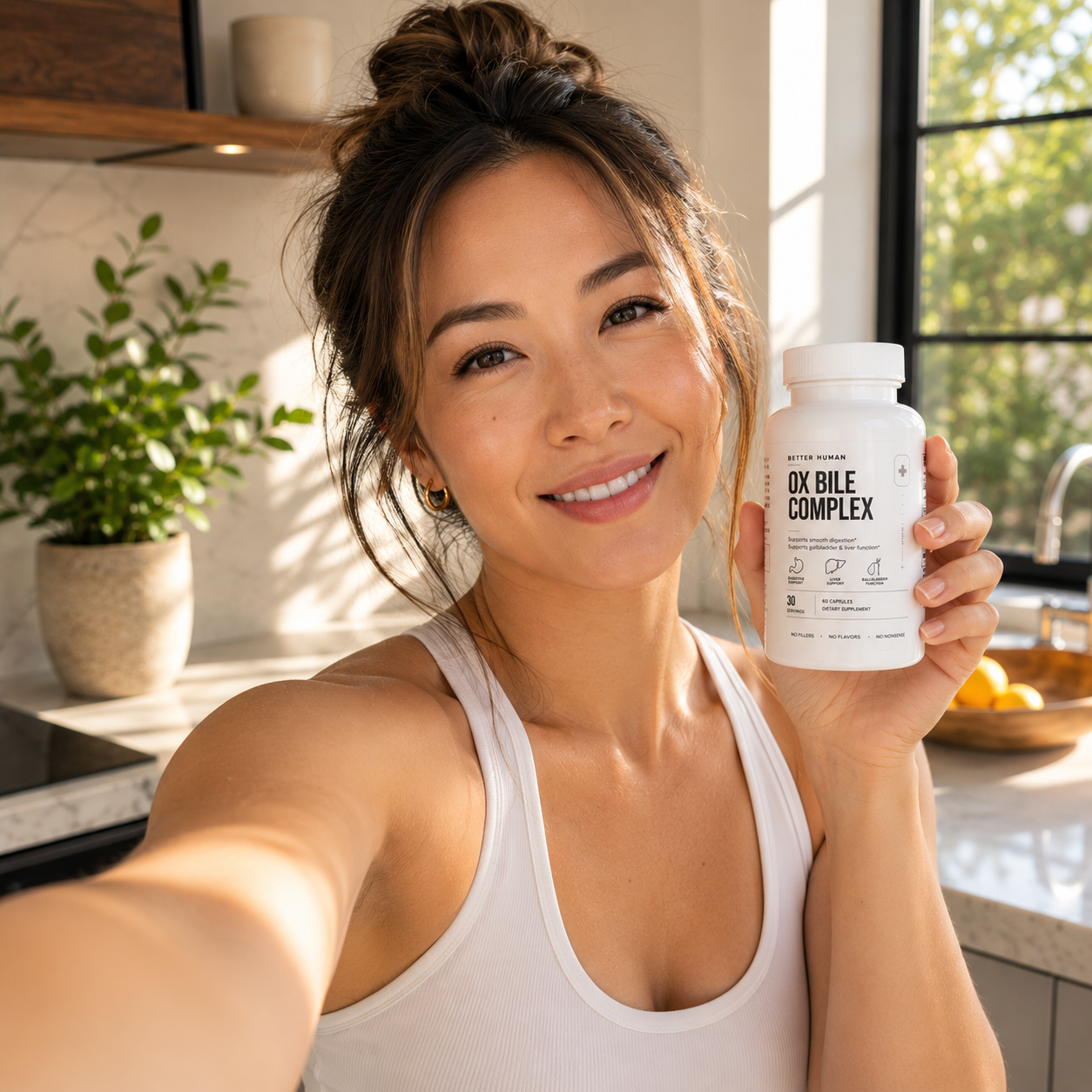 A smiling woman takes a selfie in a kitchen while holding a bottle of Ox Bile Complex supplements.