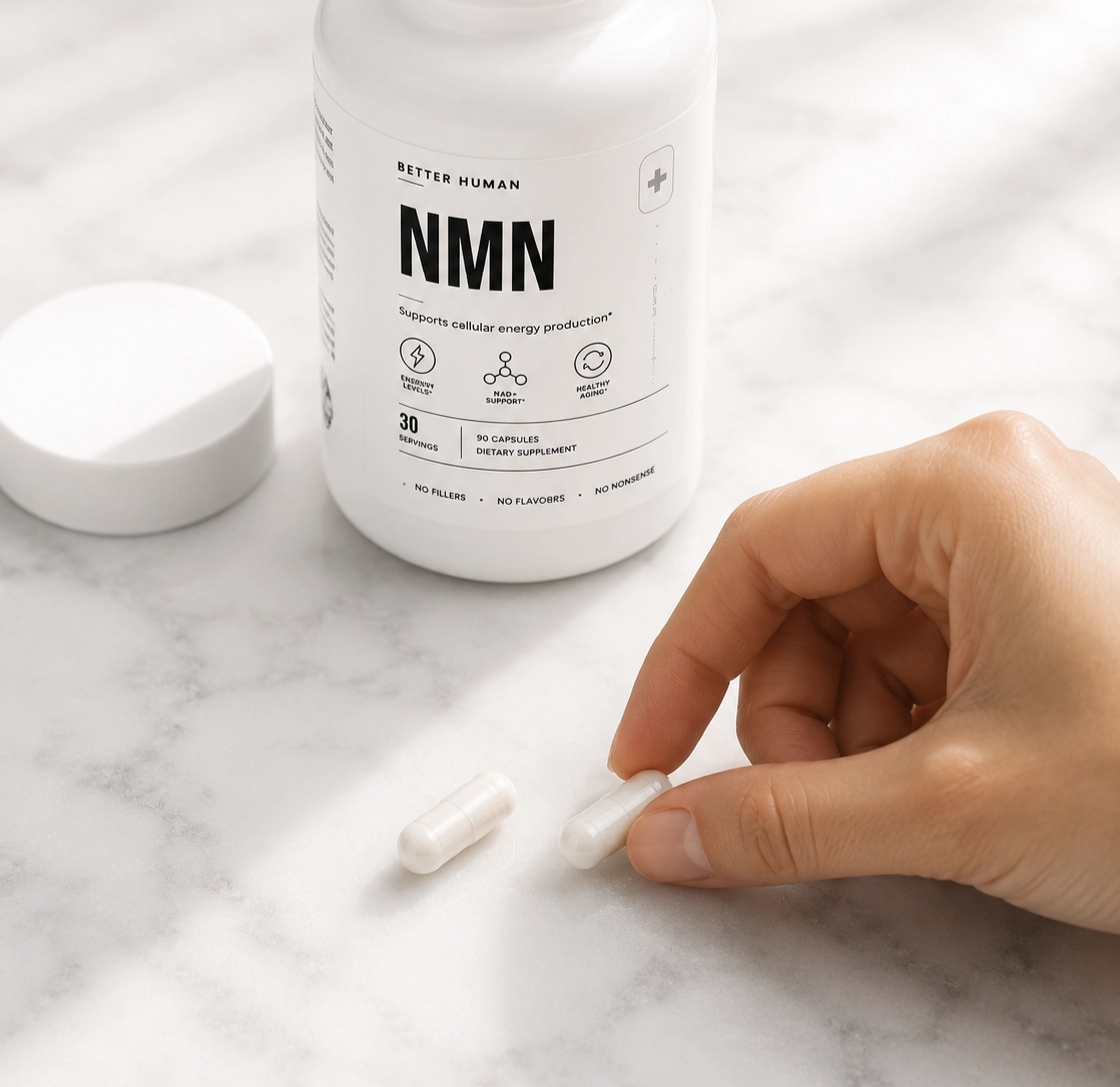 A hand holds a white capsule next to a bottle of Better Human NMN dietary supplement.