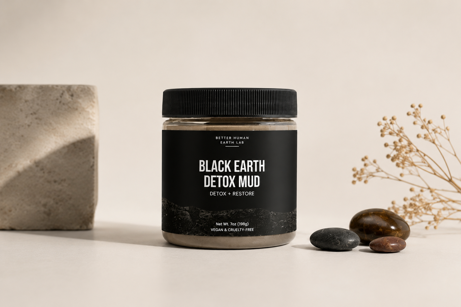 A jar of Black Earth Detox Mud sits on a surface with stones and dried flowers.