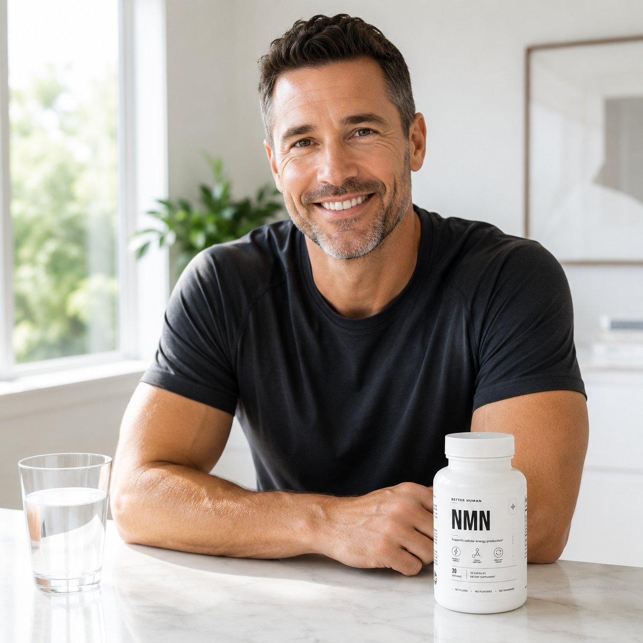 A smiling man in a black t-shirt sits at a counter with a bottle of NMN supplements.