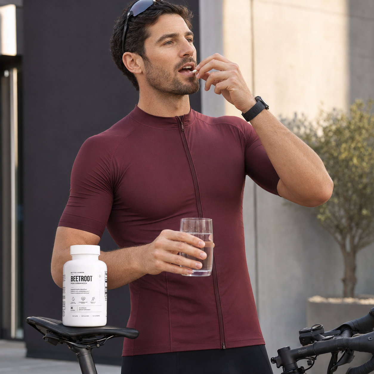 A man in cycling clothes takes a supplement pill with water, a bottle resting on his bike seat.