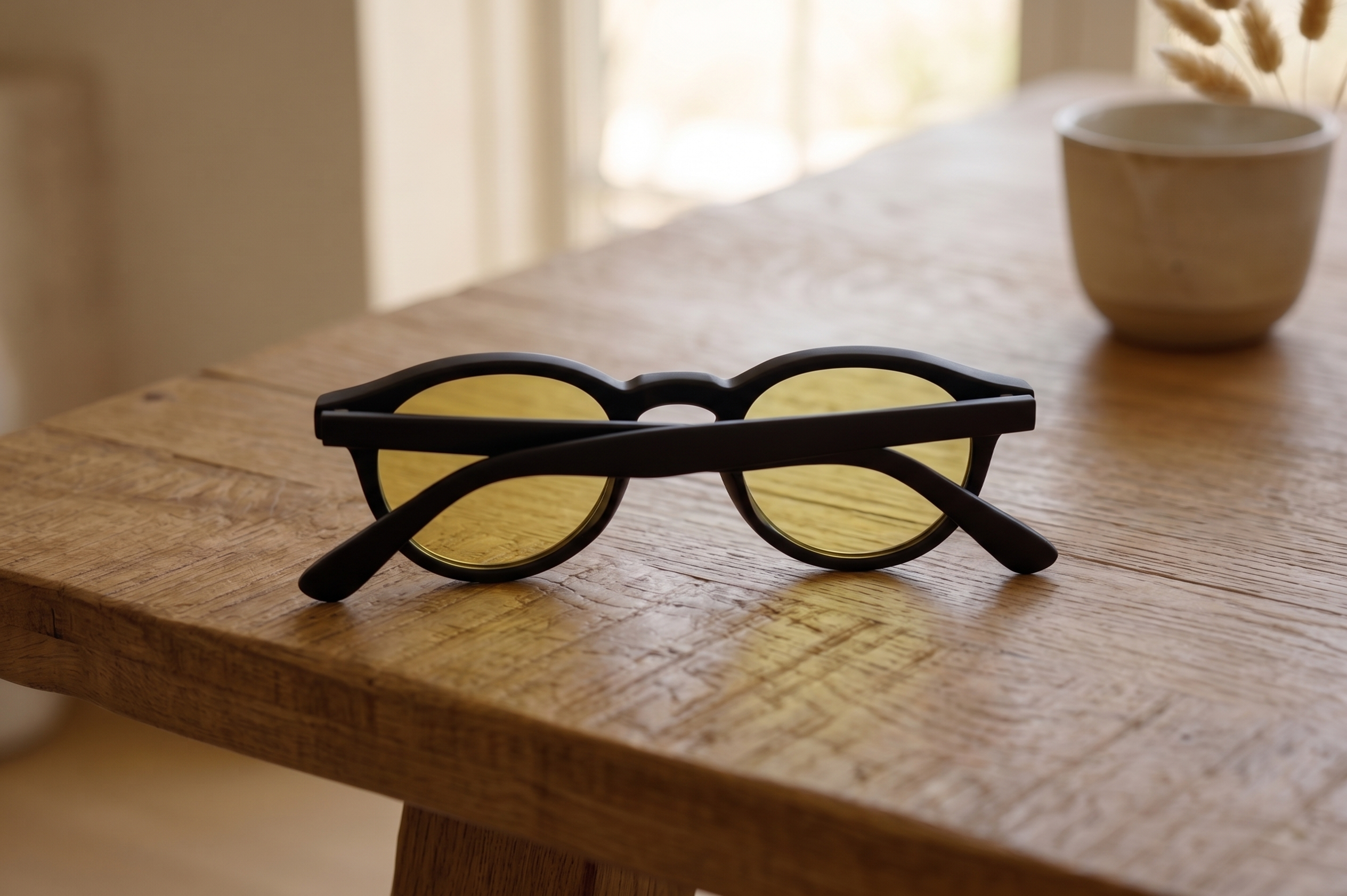 A pair of sunglasses with black frames and yellow lenses resting on a wooden table.