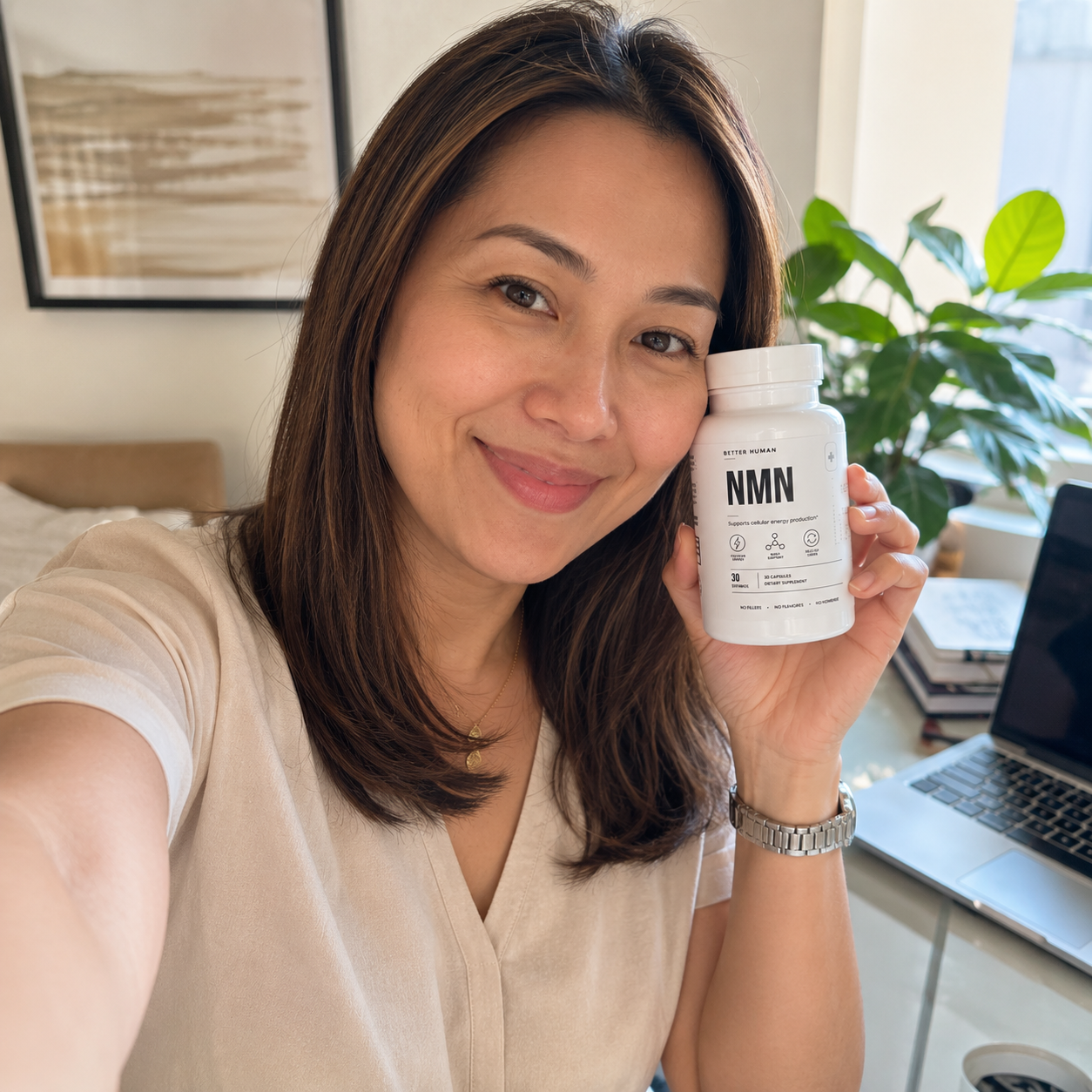 A smiling woman holds a white bottle of Better Human NMN supplements next to her face.