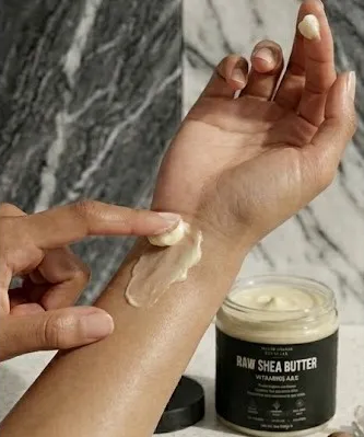 A person applying raw shea butter from a jar onto their wrist and hand.