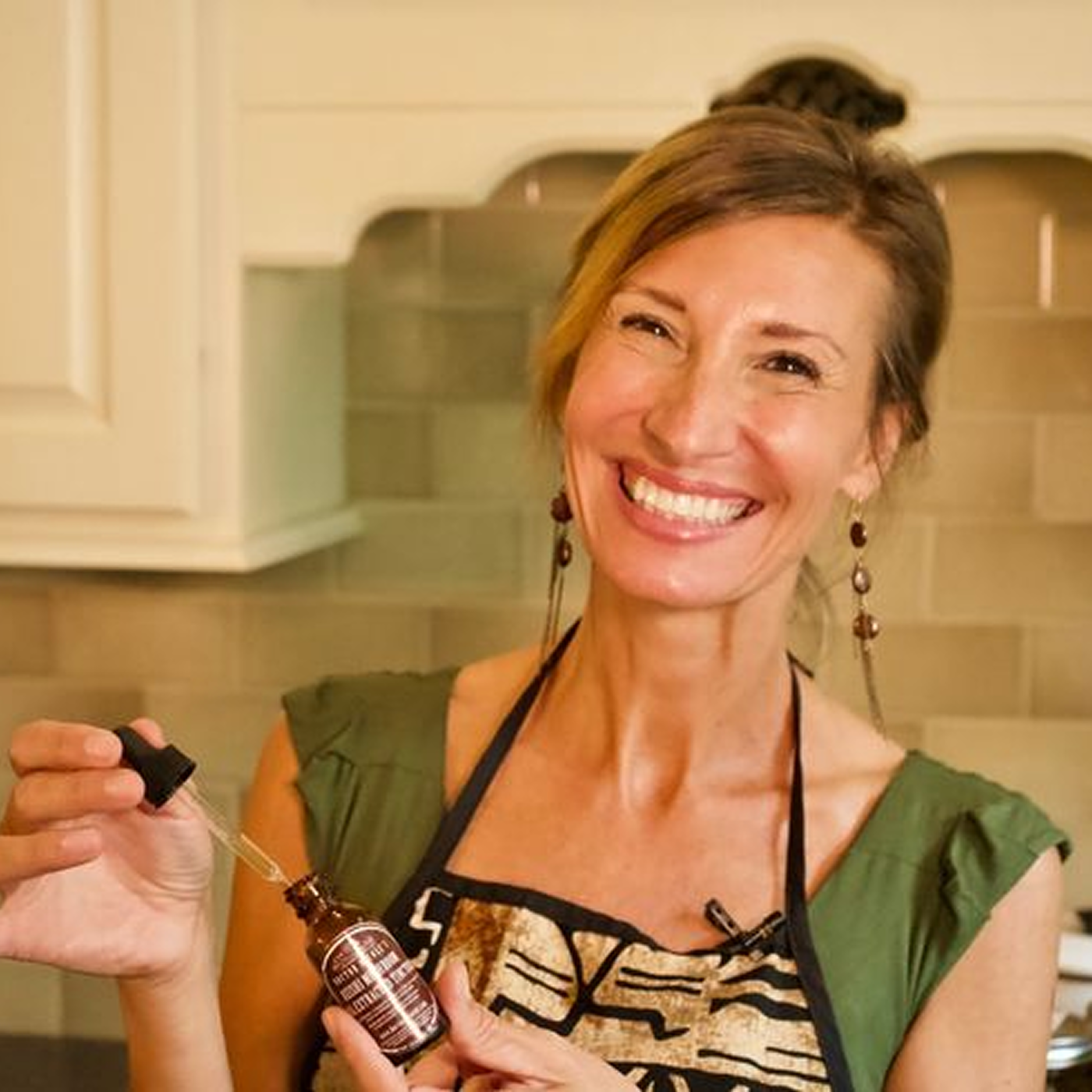 Smiling person holding a dropper bottle in a kitchen.