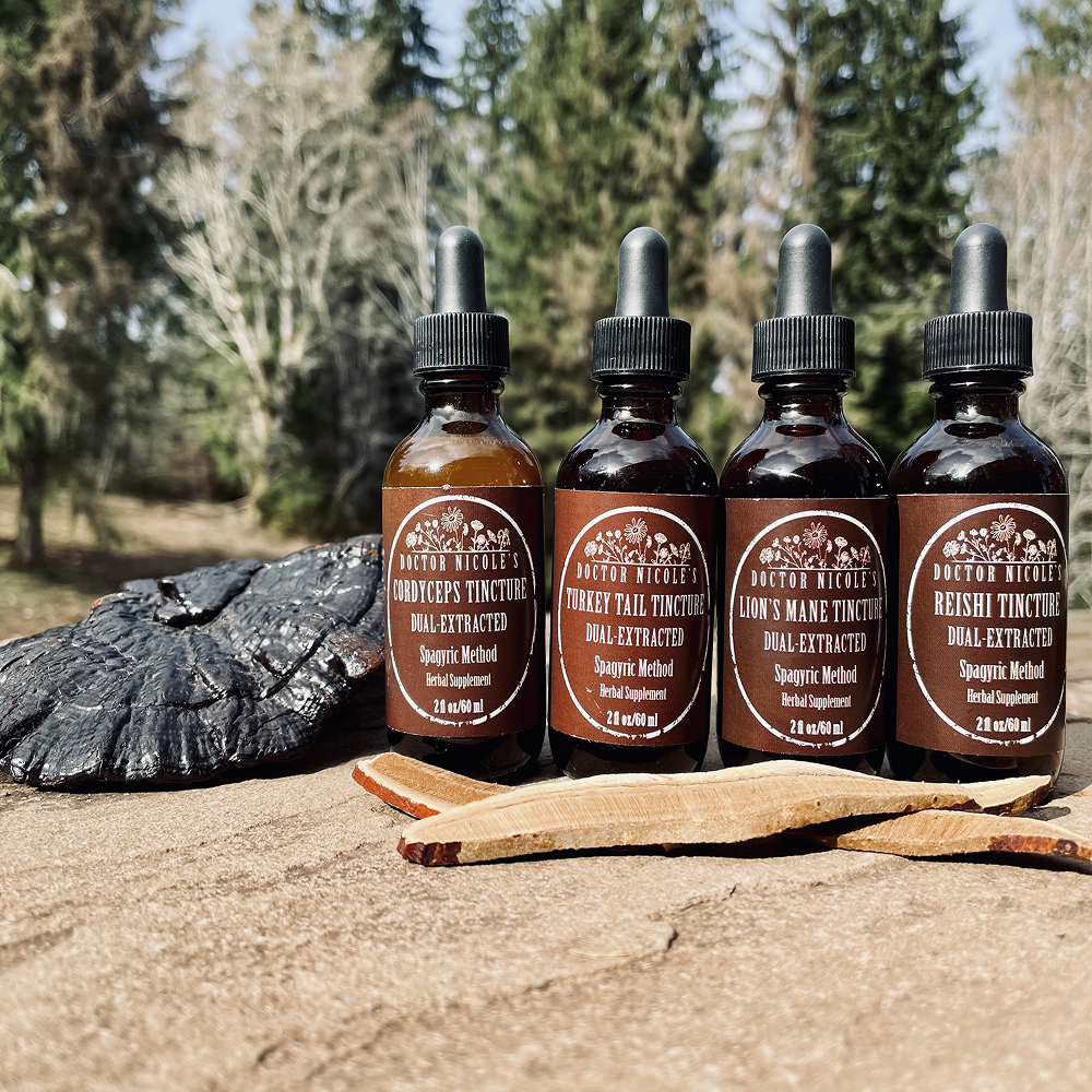 Four herbal tincture bottles on a wooden surface outdoors with a forest background.