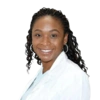 A headshot of a smiling Black woman with long, braided hair wearing a white coat against a white background.