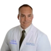 A headshot of a man in a white lab coat, white shirt, and a dark tie.