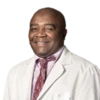 A headshot of a smiling Black man wearing a white coat, shirt, and tie.