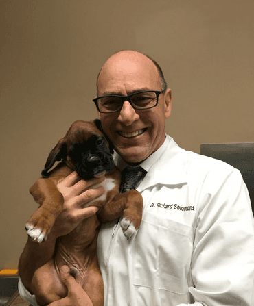 Man in white coat holding a brown puppy, smiling.