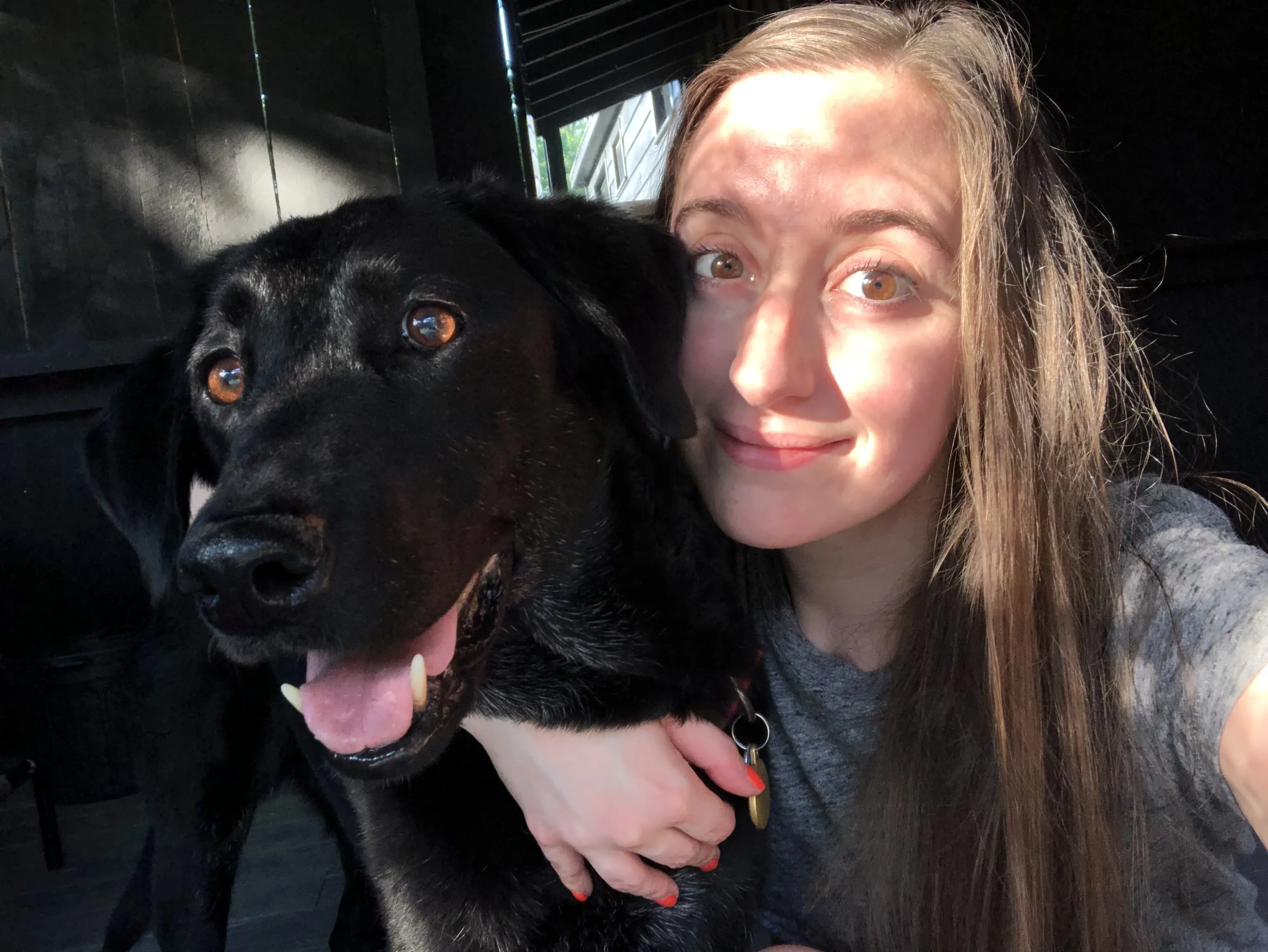 Person smiling with a black dog in sunlight.