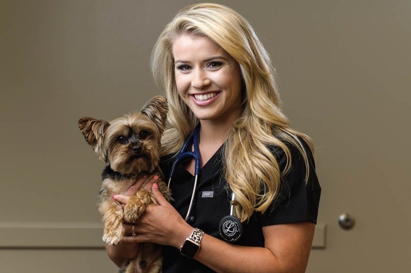 Woman in black scrubs holding a small dog, smiling.