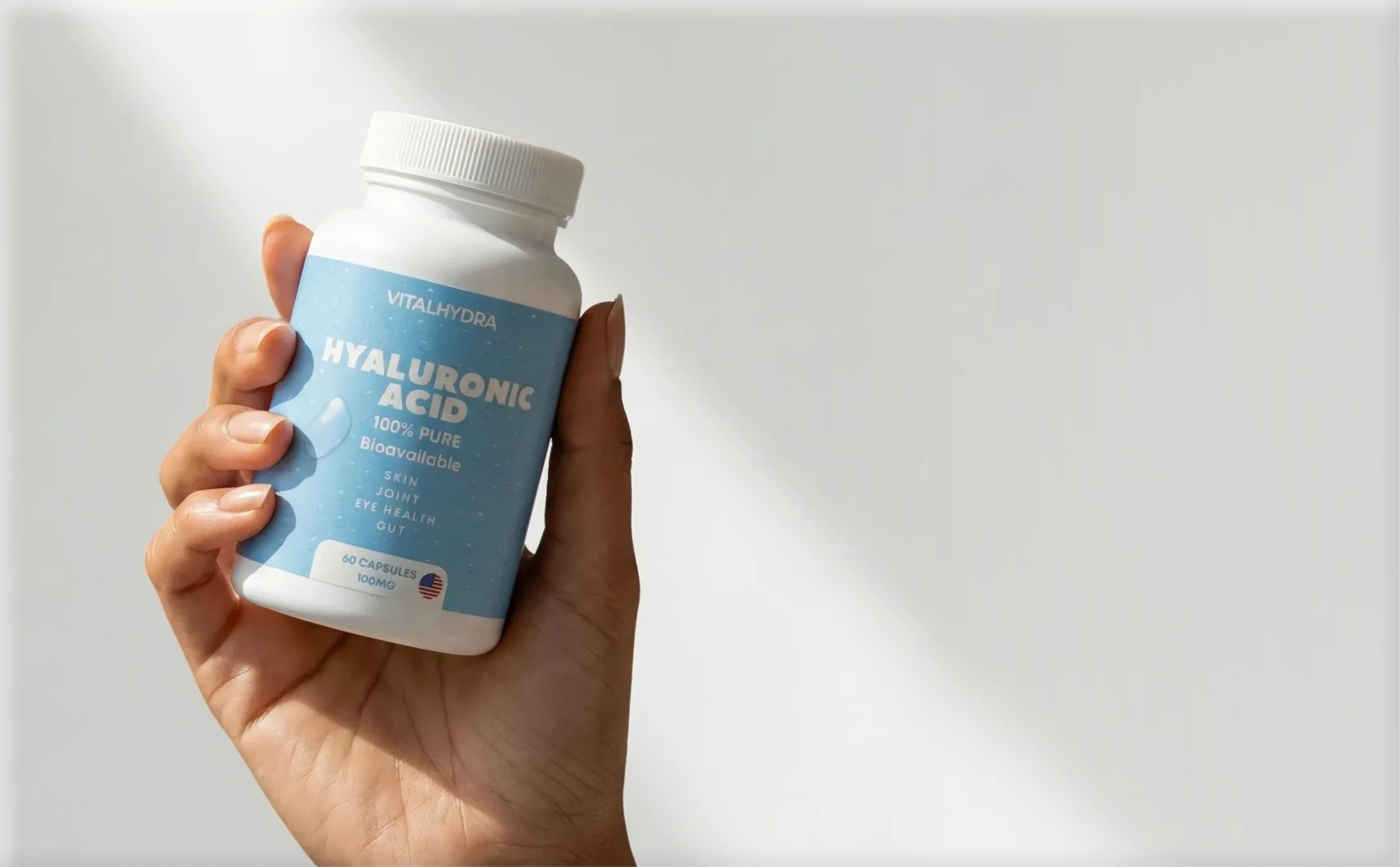 A person's hand holds a white bottle of Vitalhydra Hyaluronic Acid supplements against a white background.
