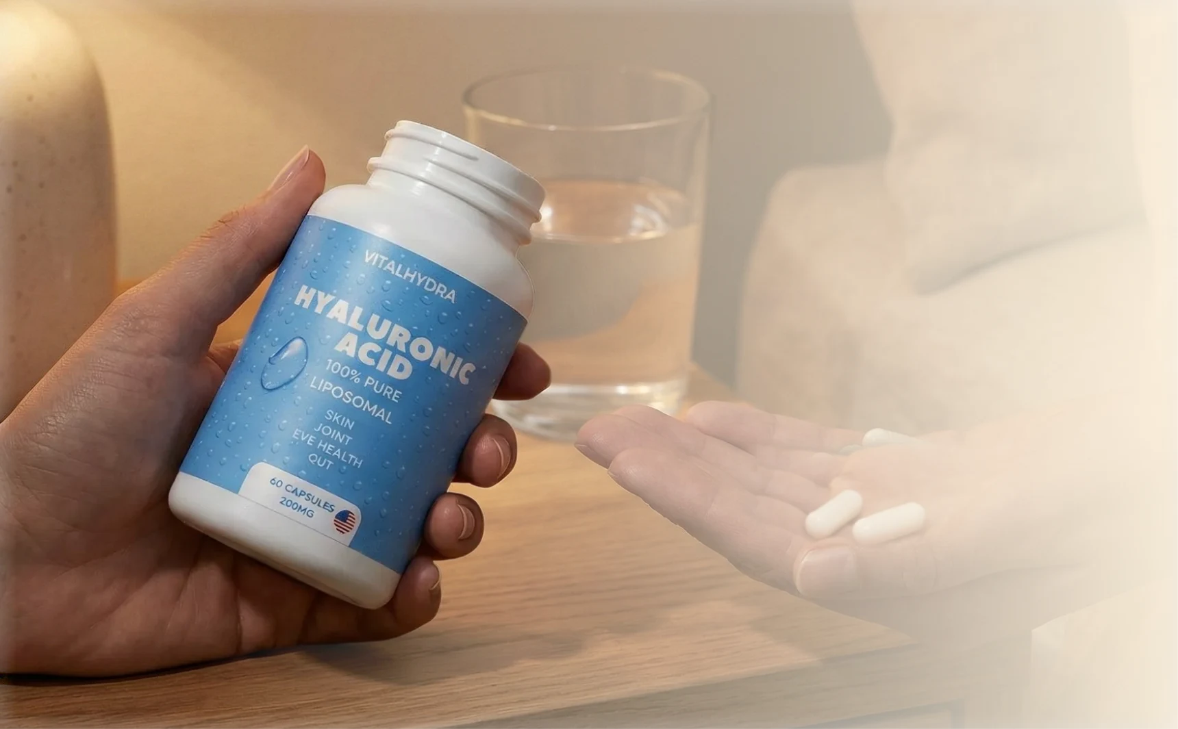 A person holds a bottle of Vitalhydra Hyaluronic Acid supplements with two capsules in their other hand.
