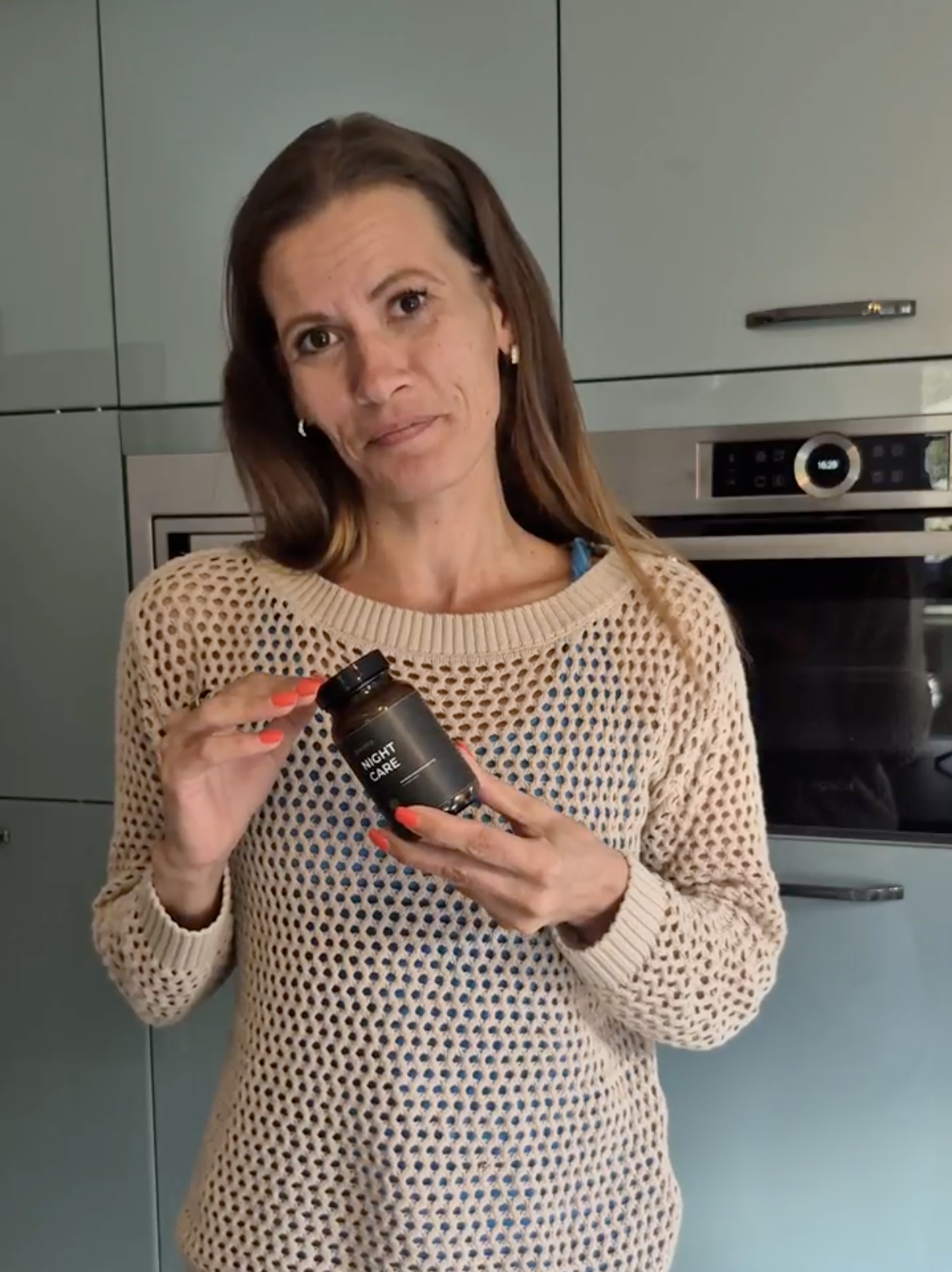 A person holding a dark bottle labeled 'Night Care' in a kitchen.