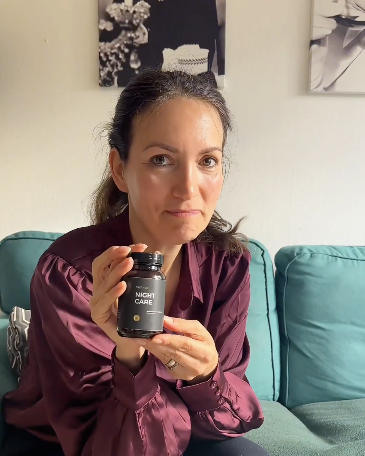 Person holding a black bottle labeled 'Night Care' seated on a teal couch.