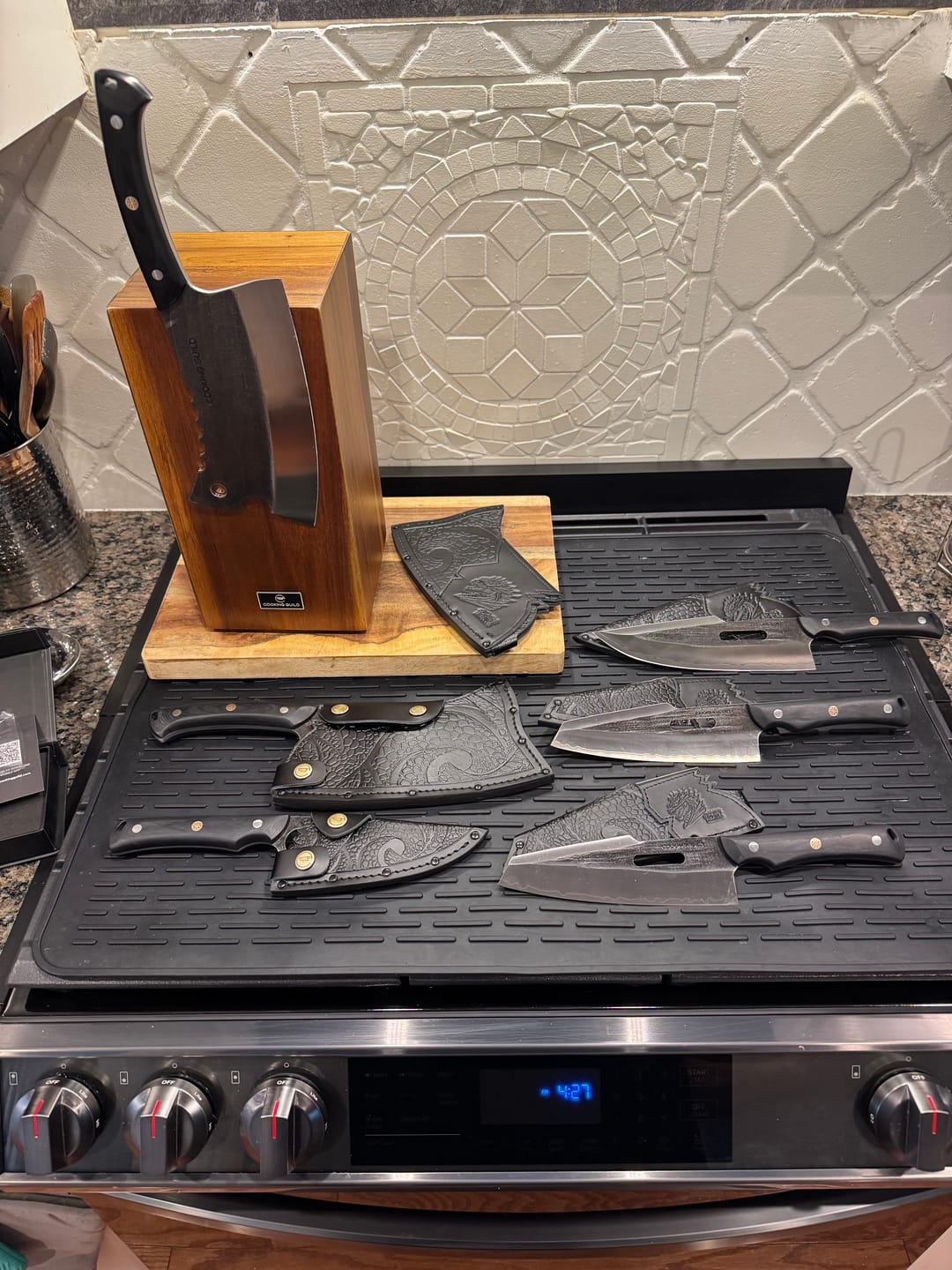 Set of knives with decorative sheaths on a stove, wooden knife block in the background.
