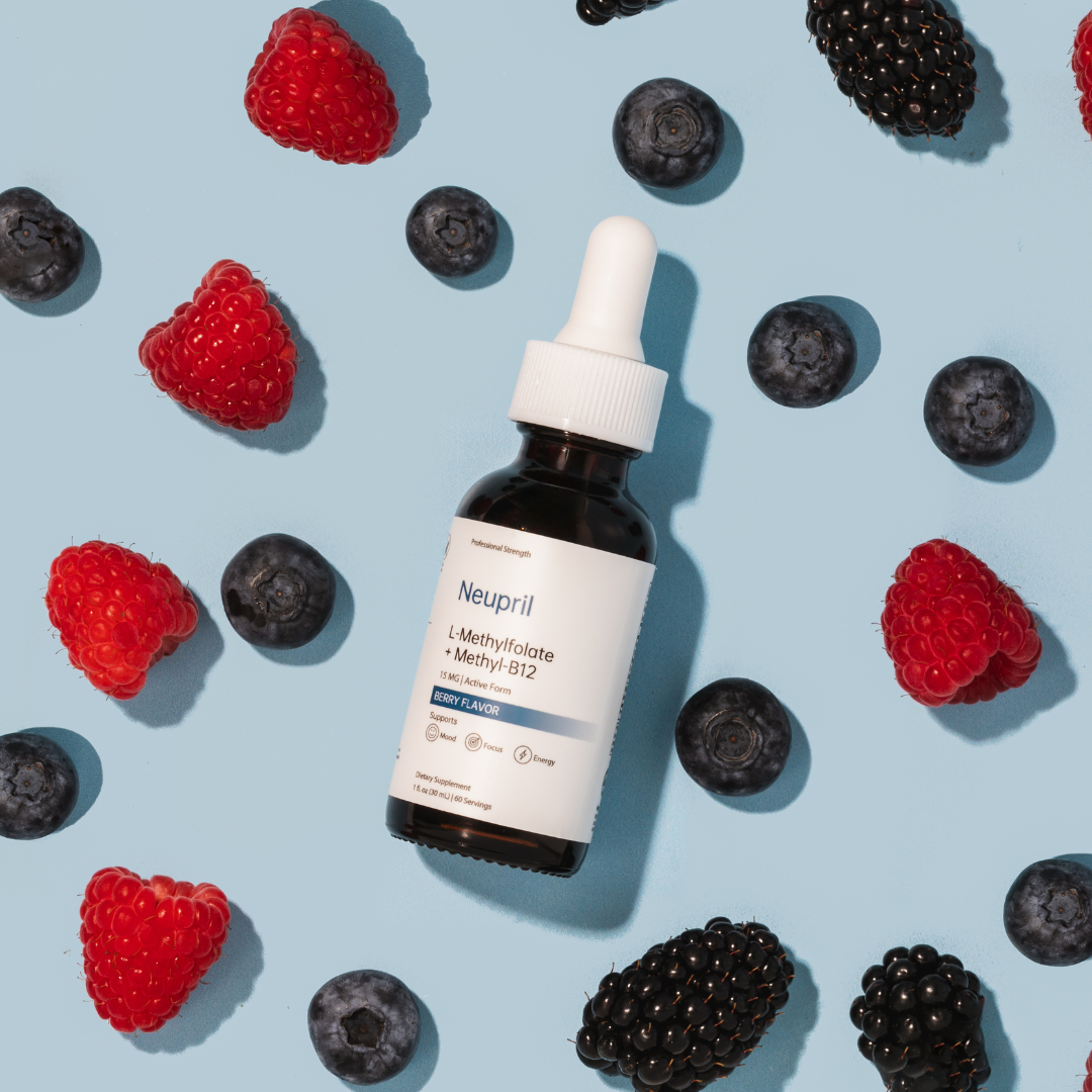 A crisp, top-down flat lay shot of a Neupril L-Methylfolate + Methyl-B12 liquid dietary supplement dropper bottle. The dark amber bottle sits on a pastel blue background, surrounded by scattered fresh raspberries, blueberries, and blackberries casting sharp shadows.