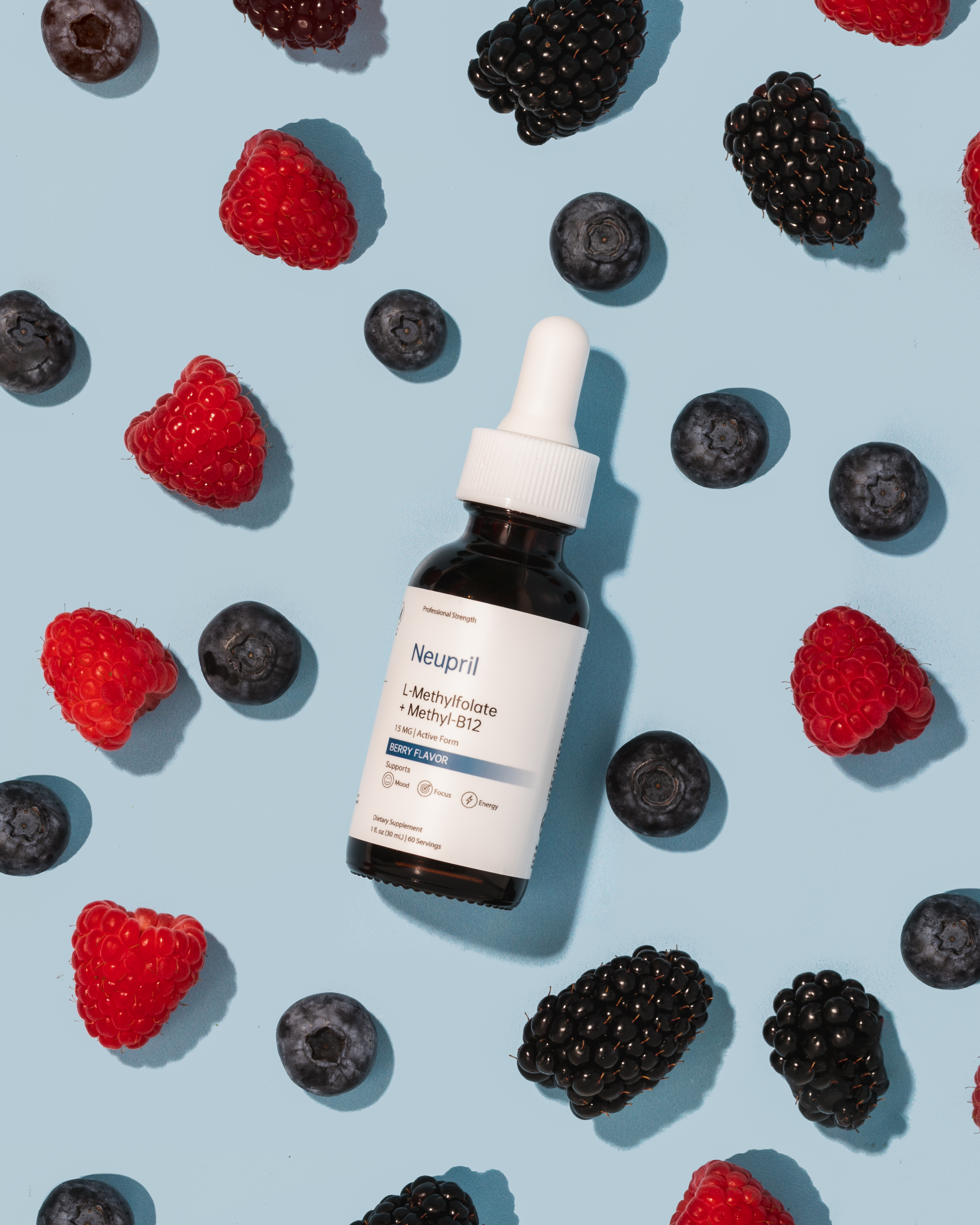 “A bottle of Neupril L-Methylfolate + Methyl-B12 supplement with a white dropper lies on a light blue background surrounded by fresh raspberries, blackberries, and blueberries, highlighting its berry flavor