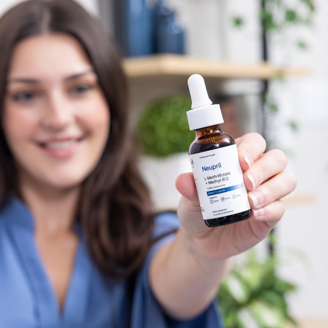 A smiling woman holds up a bottle of Neupril L-Methylfolate + Methyl-B12 supplement with a dropper, showcasing it toward the camera in a bright, modern indoor setting
