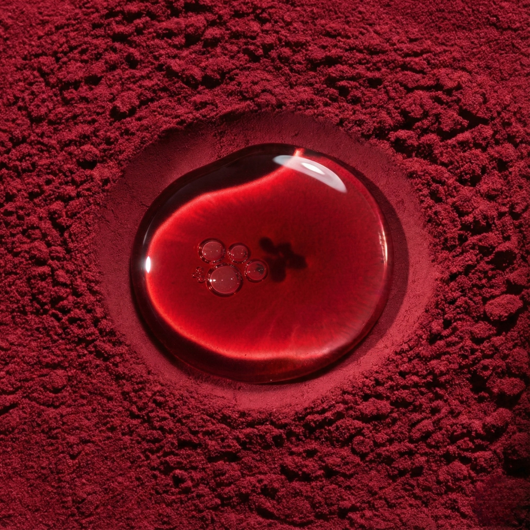 Close-up of a red methylfolate liquid droplet resting on powdered nutrients.