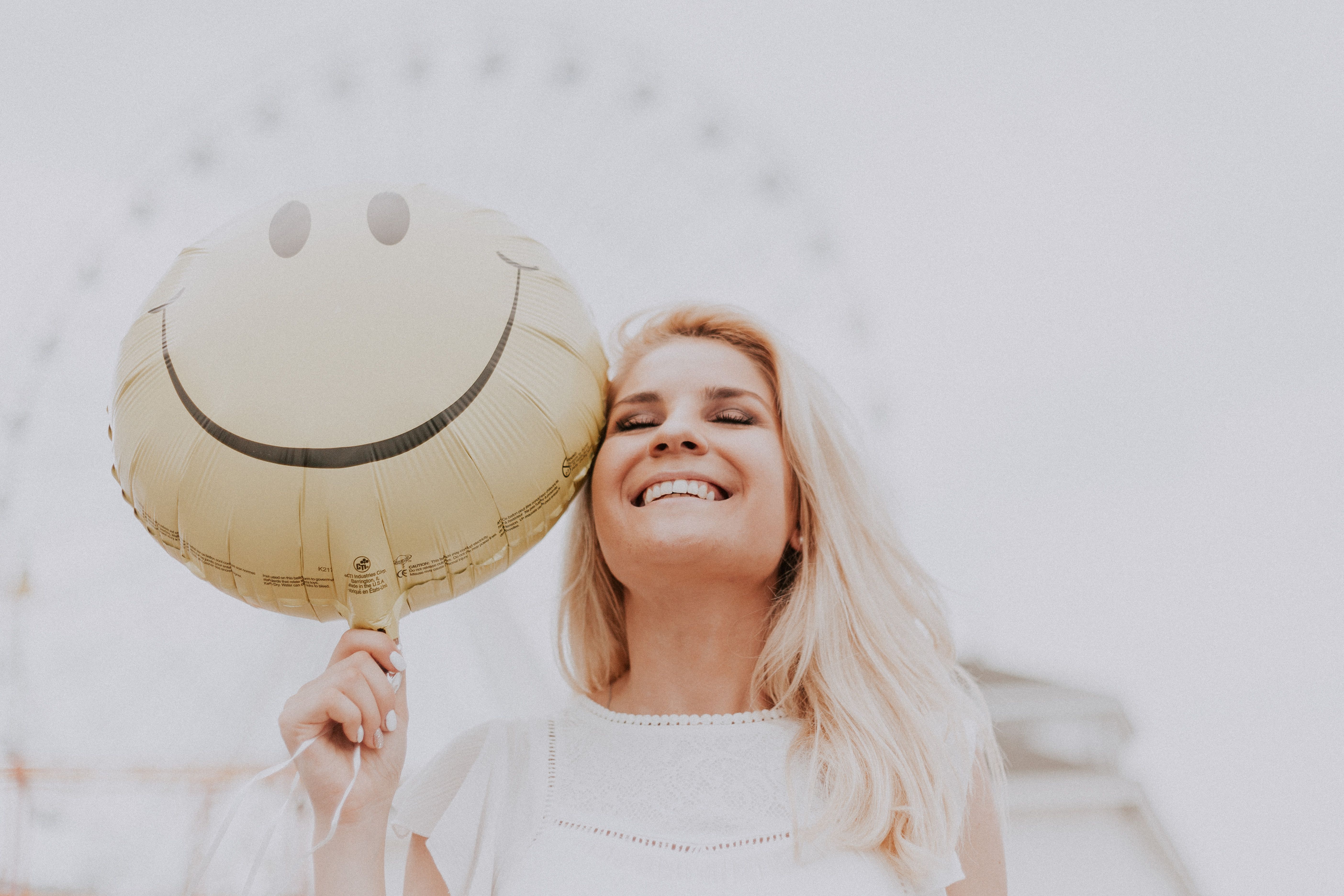 A woman with blonde hair smiling while holding a smiley face balloon after trying supplements for mood support