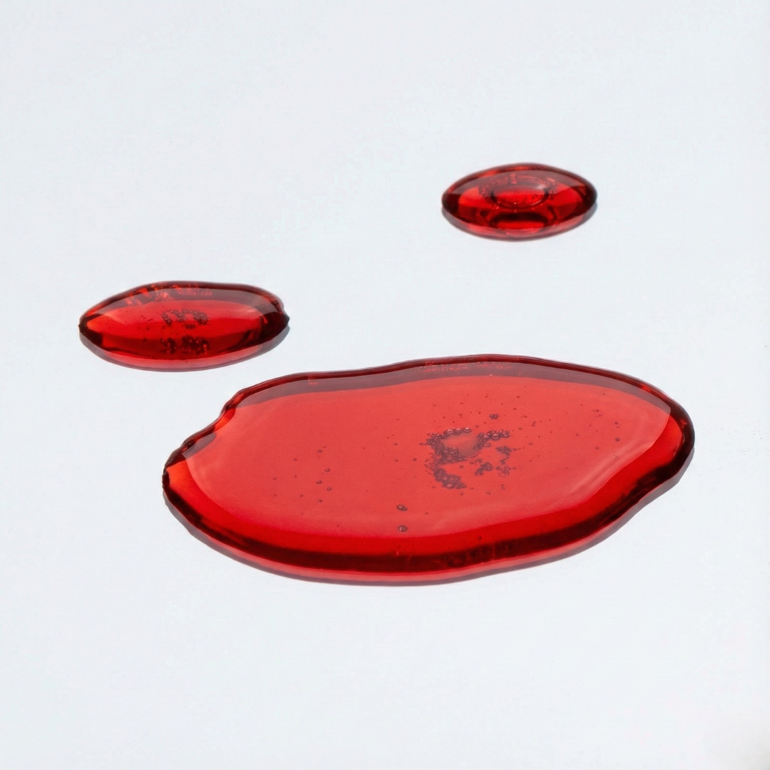 Three glossy red methylfolate droplets on a smooth white surface