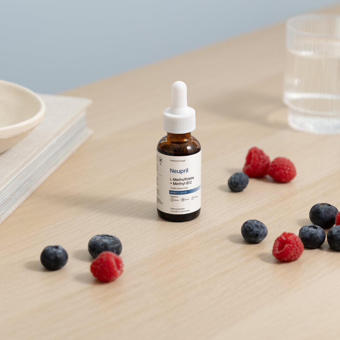 A bottle of Neupril L-Methylfolate + Methyl-B12 liquid supplement centered on a light wooden table, surrounded by scattered fresh blueberries and raspberries with a glass of water in the blurred background.