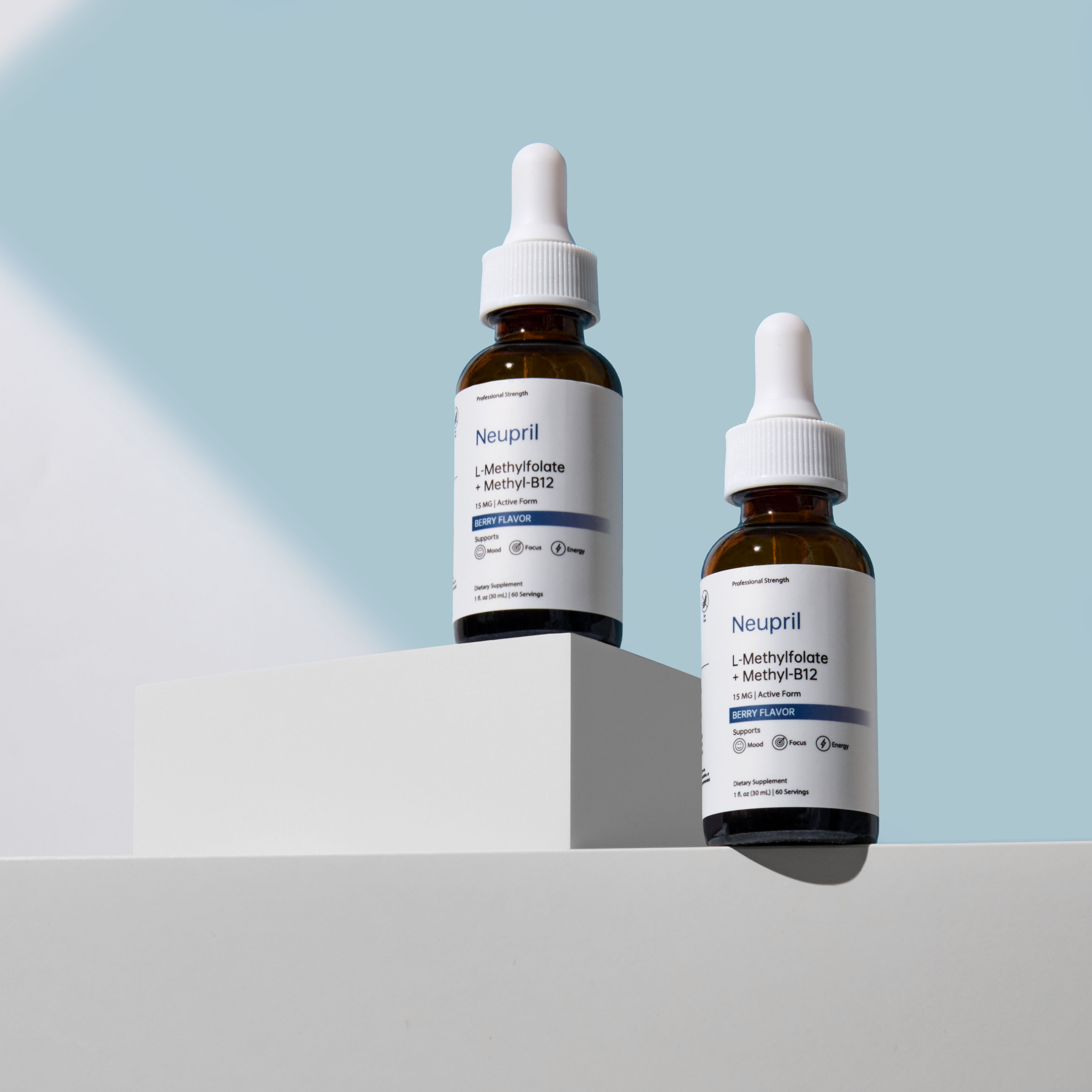 Two bottles of Neupril L-Methylfolate + Methyl-B12 supplement with white droppers displayed on minimalist white platforms against a soft light blue backgroun