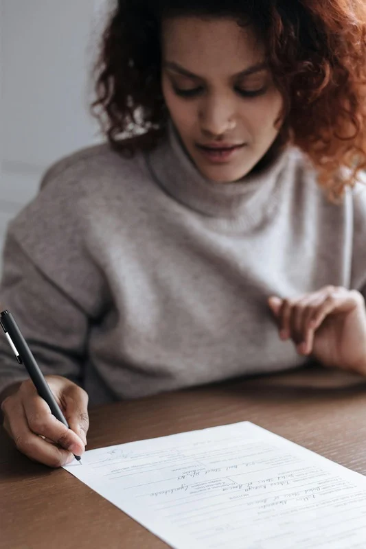 Person writing on a document at a wooden table.