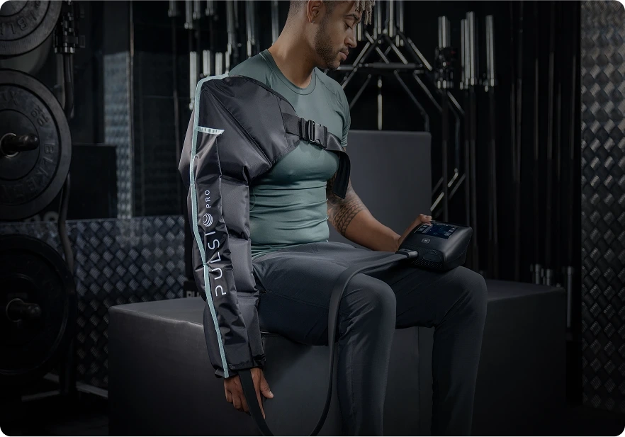 Person using an arm compression therapy device in a gym setting.