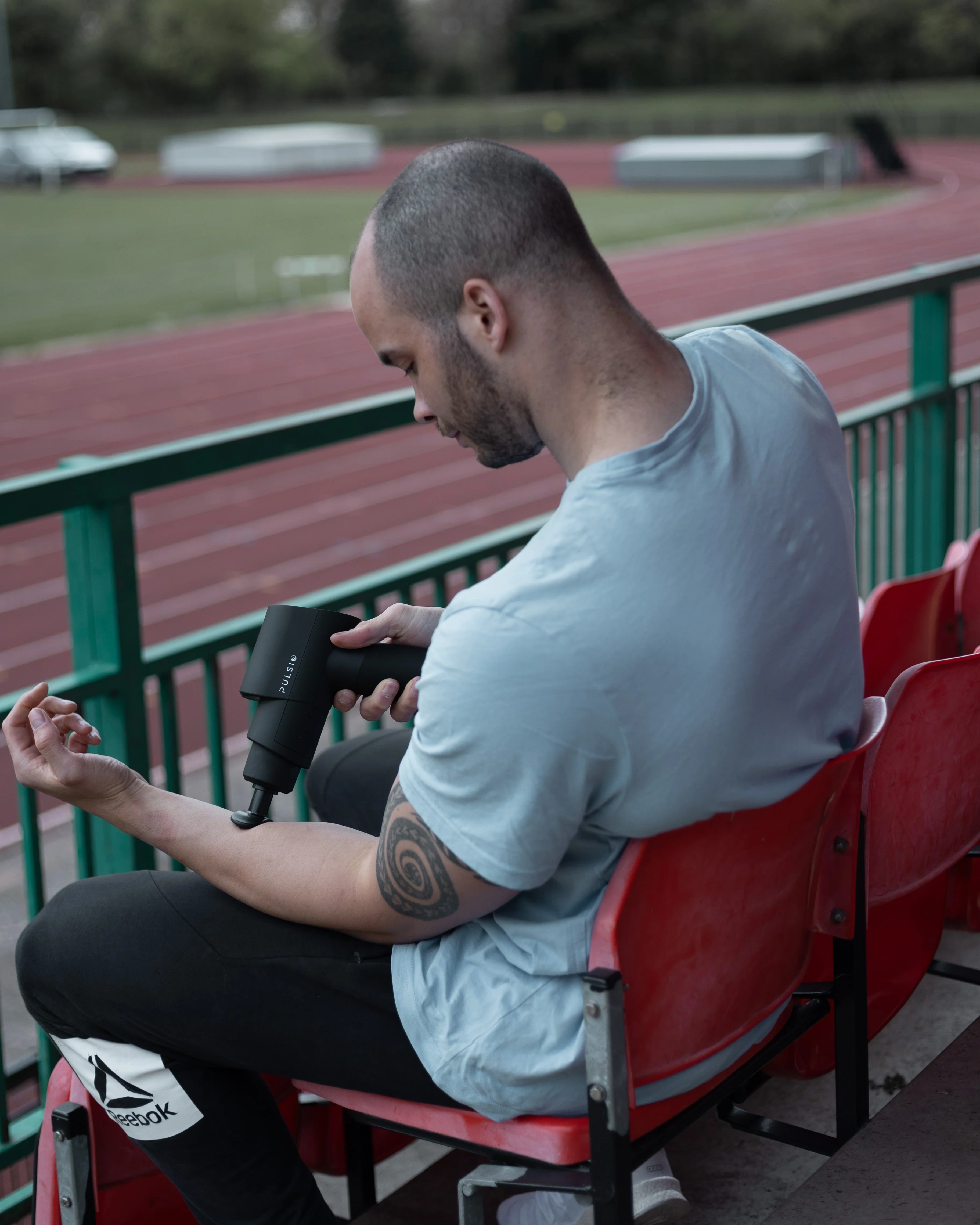 Person using a massage gun on their arm seated at a stadium.