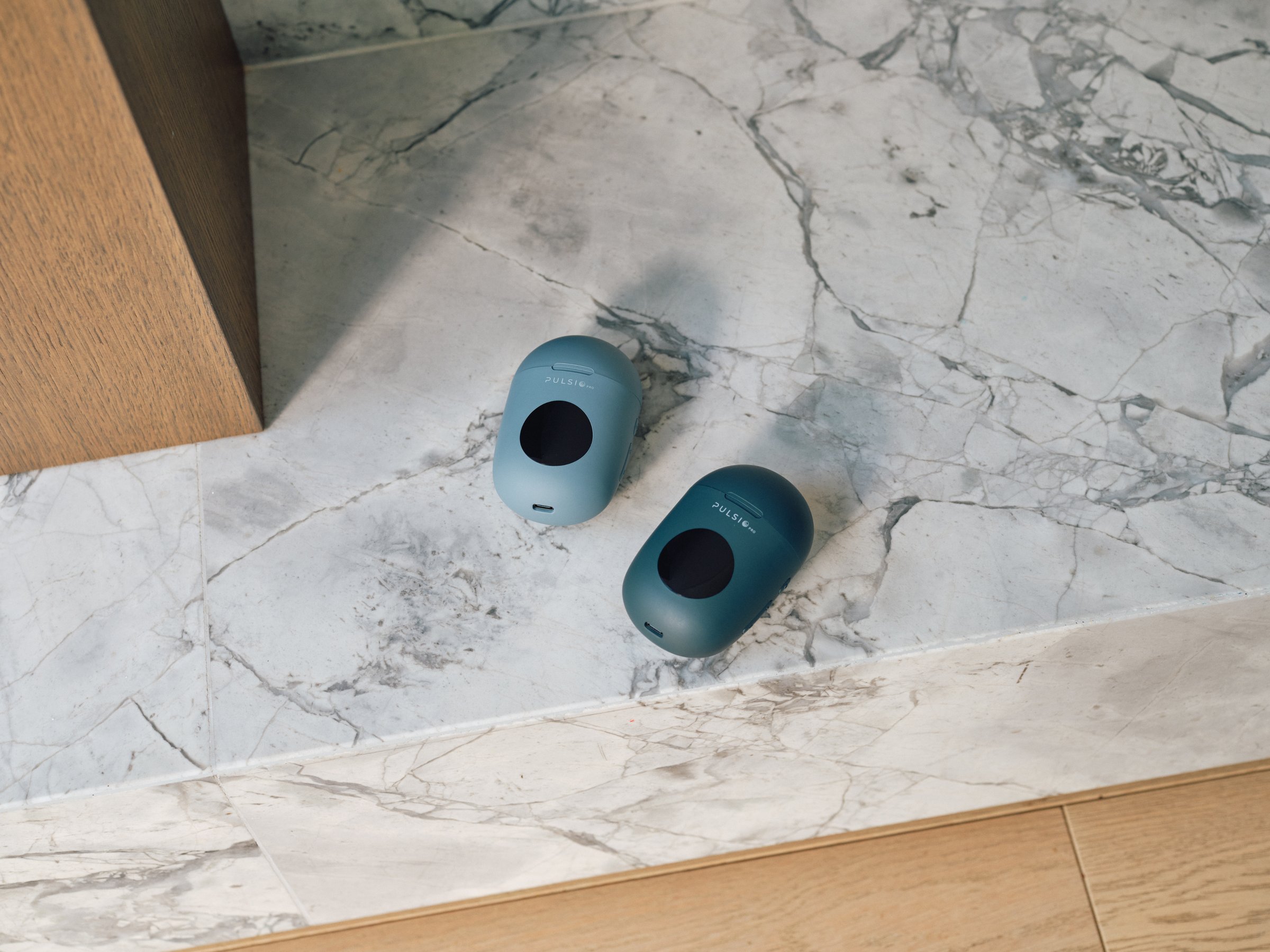 Two blue Pulsio Pro devices resting on a white marble surface next to a wooden floor and cabinet.
