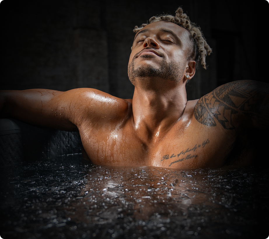 A man with tattoos relaxes in an ice bath, eyes closed.