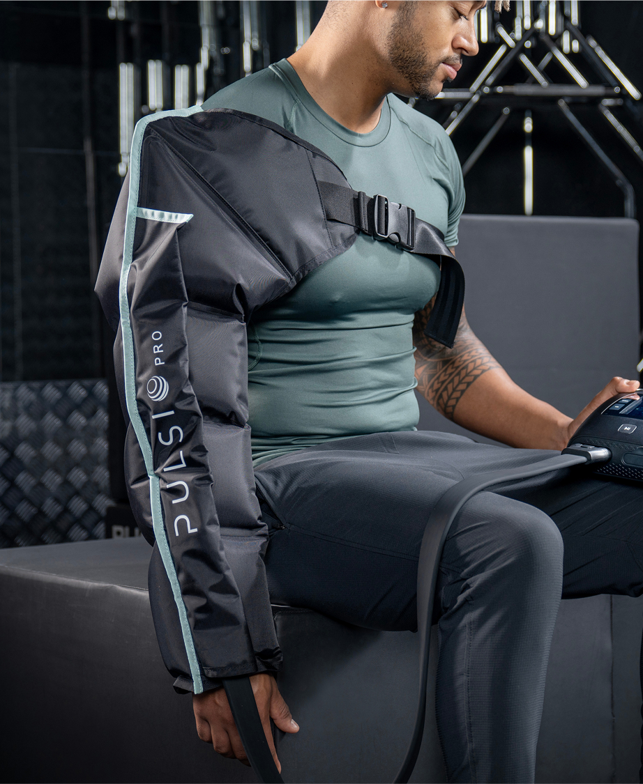 Person using arm compression therapy device in a gym setting.
