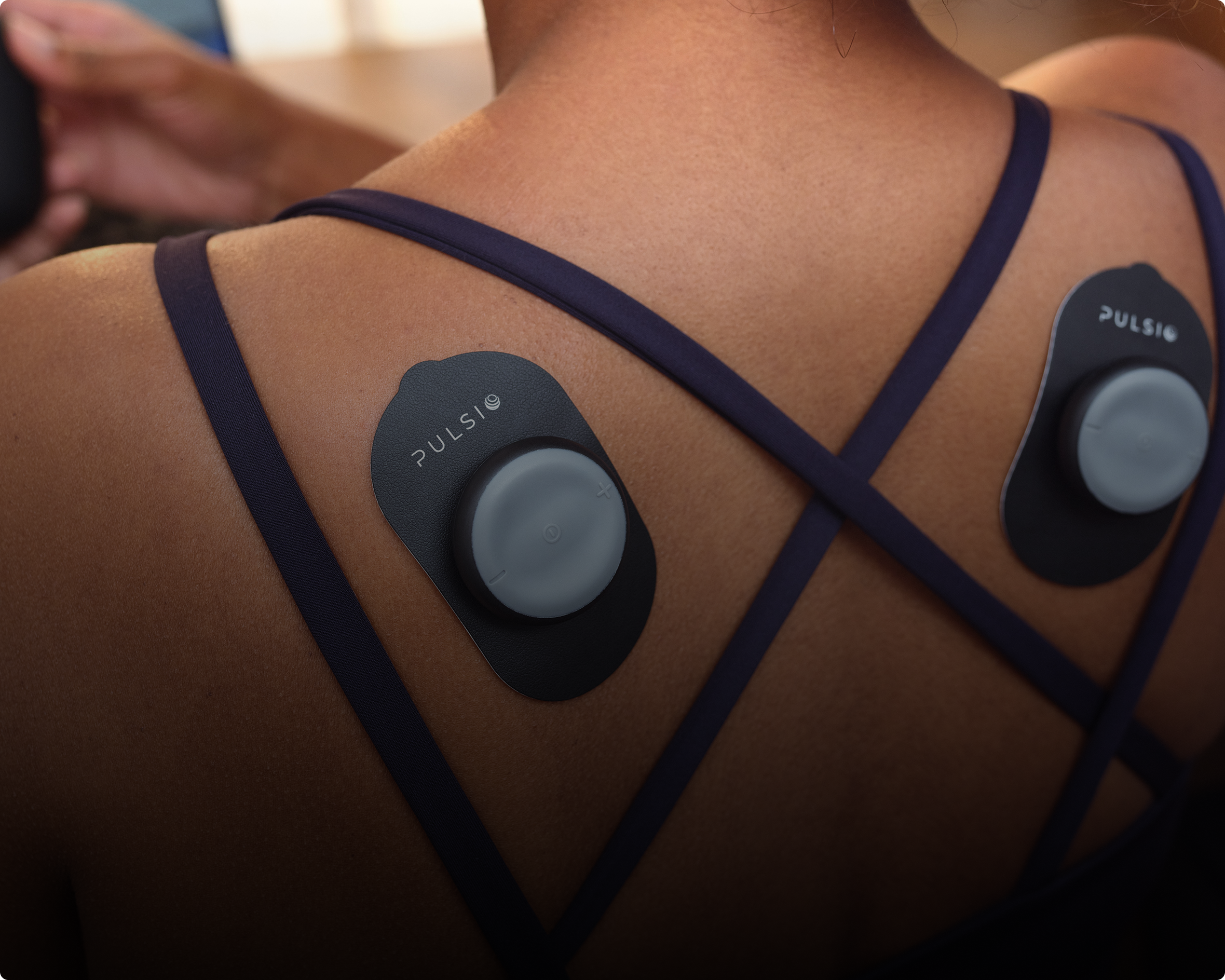 A close-up of a person's back with two Pulsio devices attached to their skin on the shoulder blades.