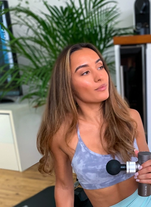 Person holding a massage device, sitting in a room with plants and furniture.