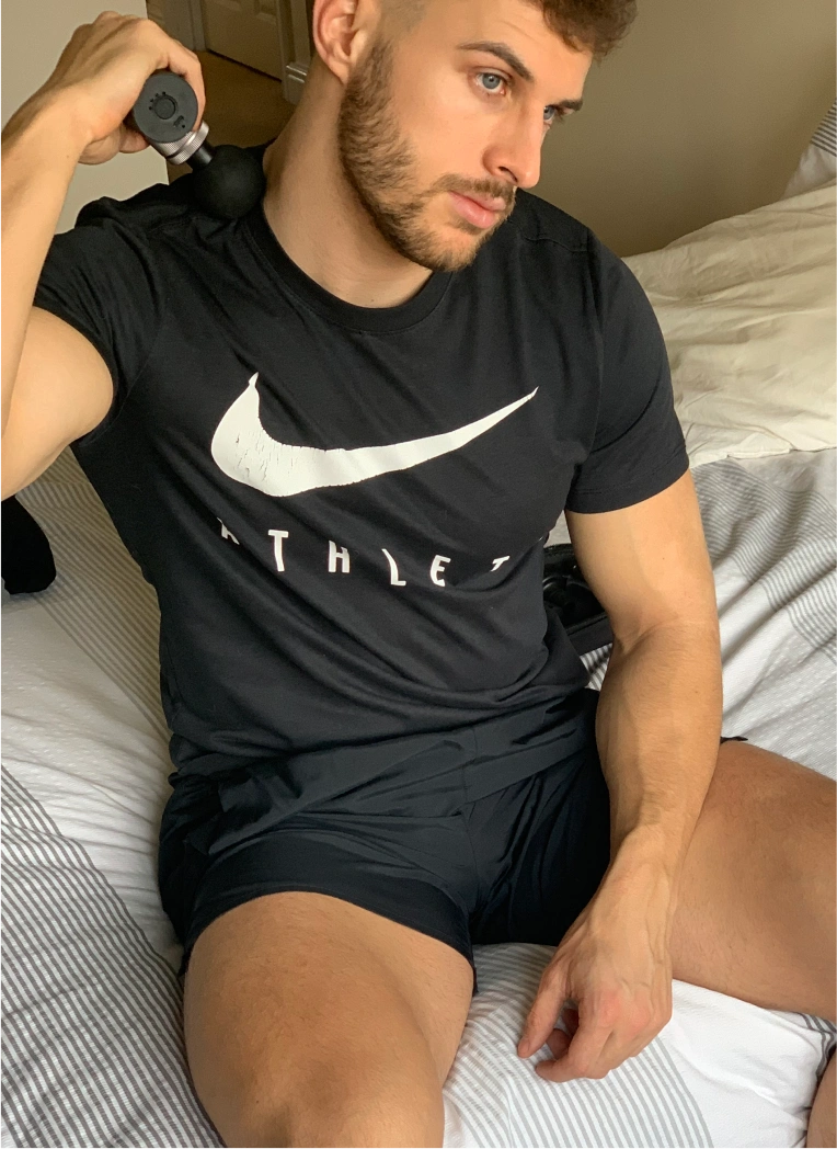 Person using a massage device on shoulder, wearing black athletic shirt.