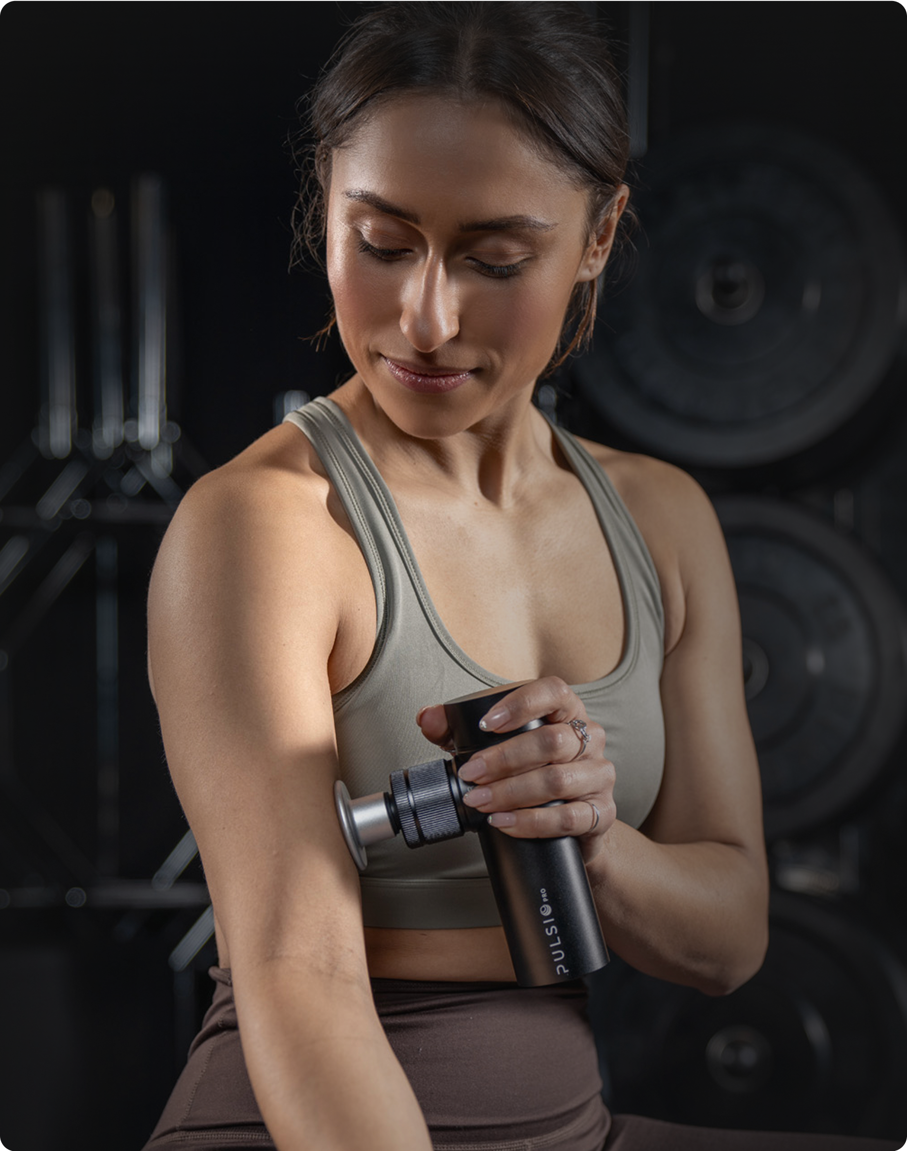 Woman using a massage gun on her arm in a gym setting.