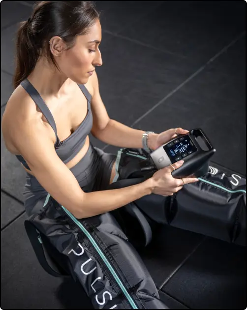 Person using compression therapy device on legs, holding a control unit.
