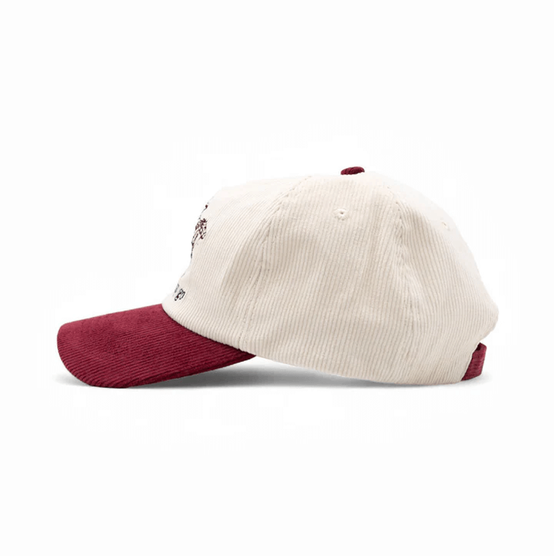 A side view of a cream-colored corduroy baseball cap with a maroon brim, set against a white background.