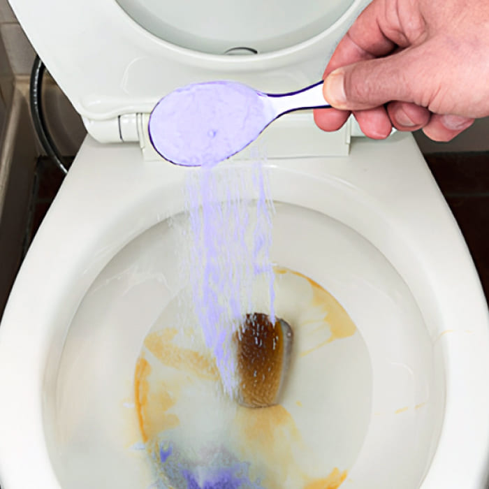 Hand pouring purple powder into a toilet bowl.