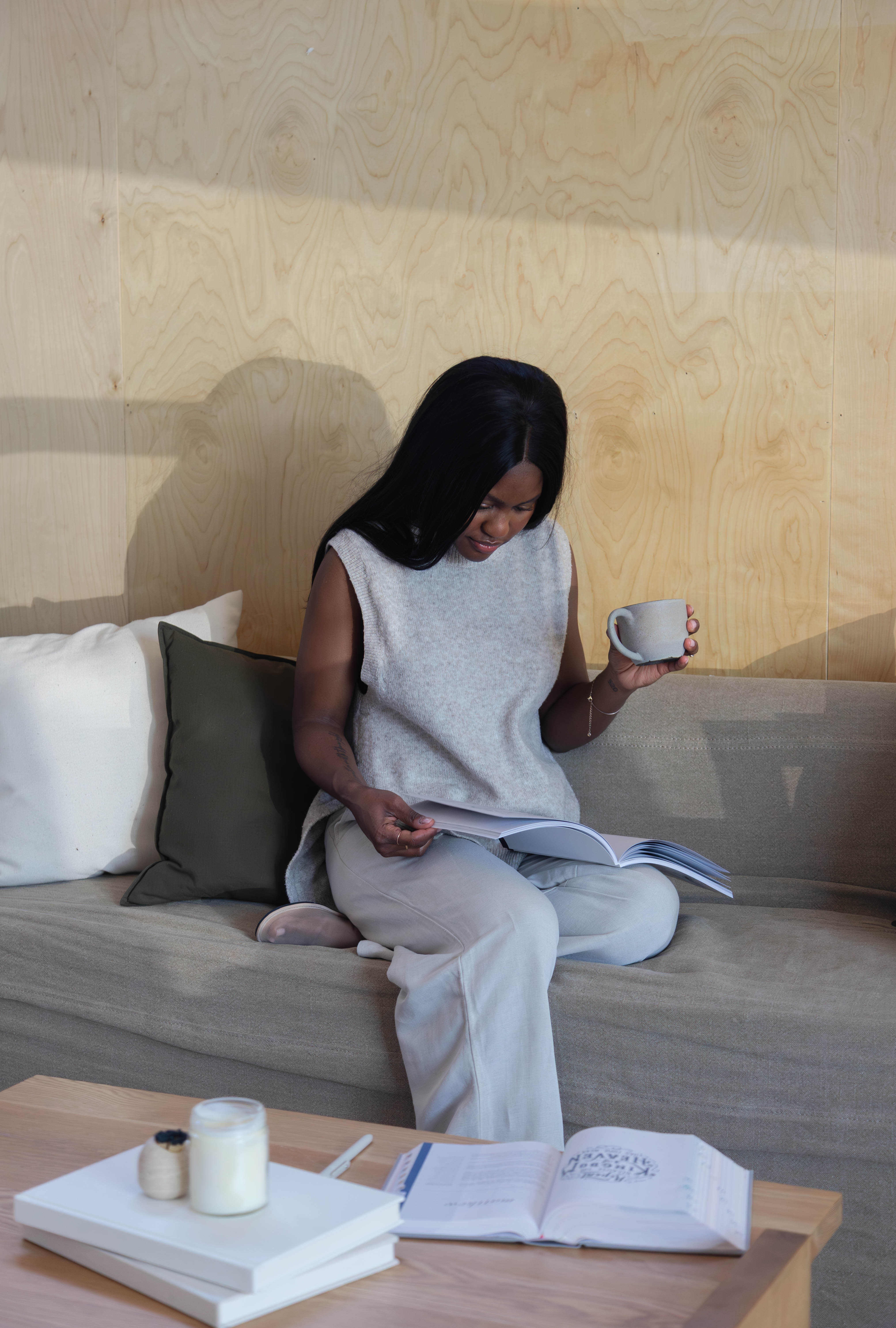 Person sitting on a couch, reading a book and holding a mug.