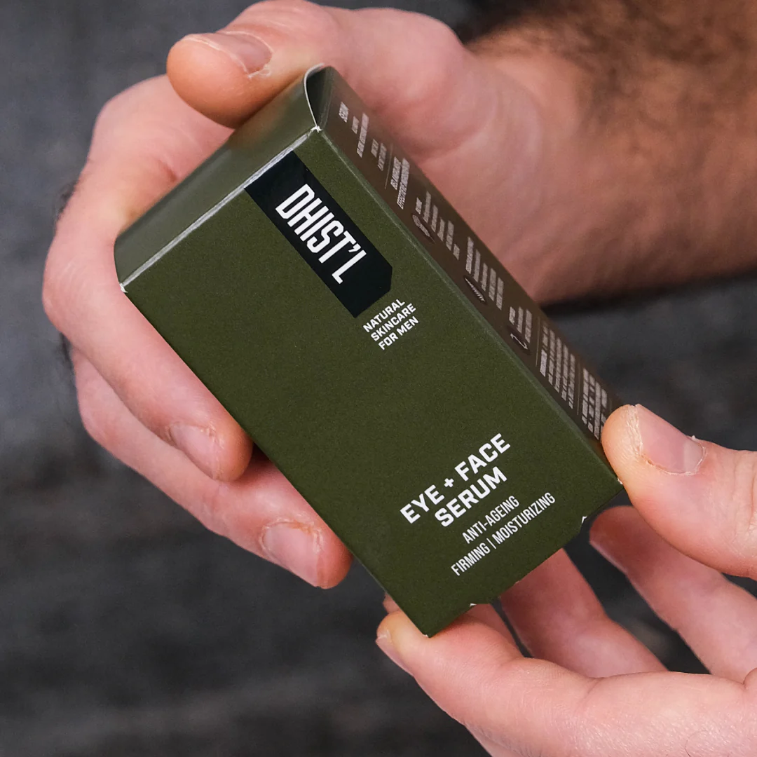 Hands holding a green box labeled 'Eye + Face Serum' for men.