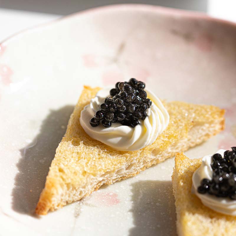 Two toast triangles with cream and black caviar on a plate.