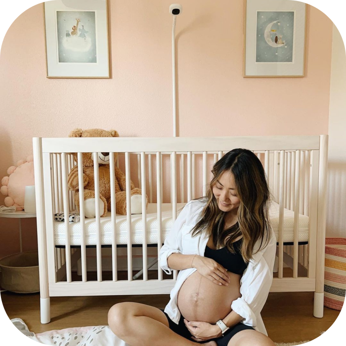 A pregnant woman sits on the floor of a nursery, holding her belly in front of a crib.