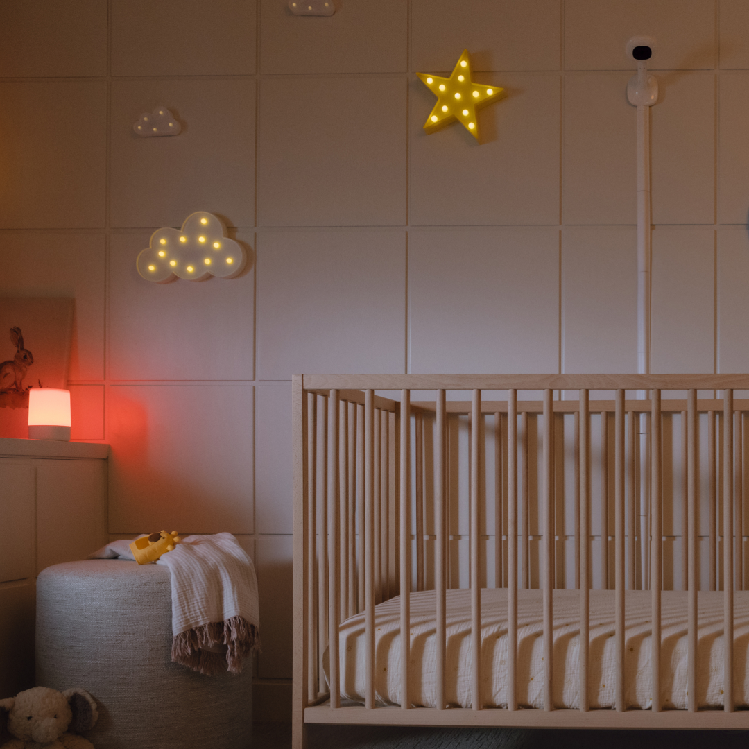 A nursery at night with a wooden crib, decorative wall lights, and a red night light.