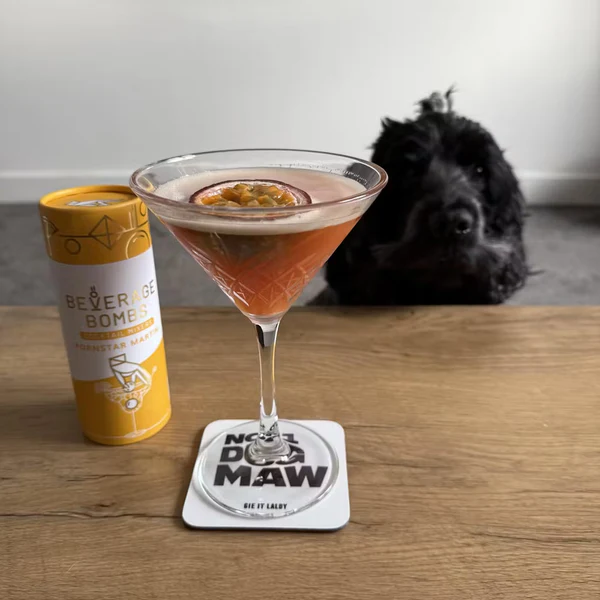 Cocktail glass with passion fruit, beverage can, and a black dog in the background.