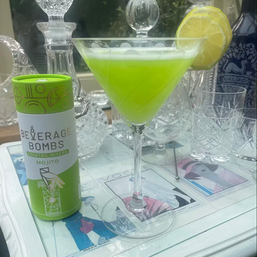 Green cocktail in a martini glass with lemon slice, next to a mojito mixer can.