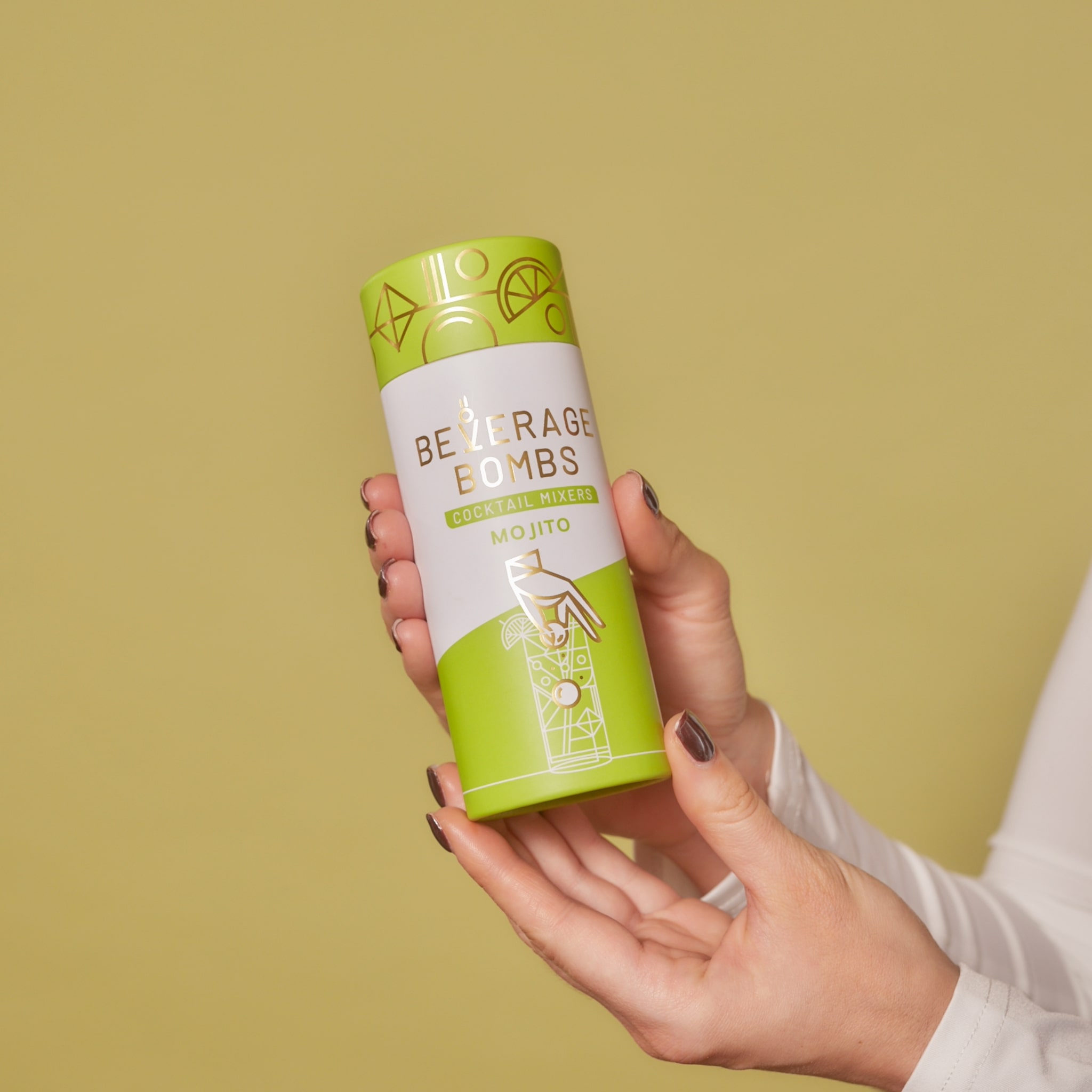 A pair of hands holding a tube of Beverage Bombs Mojito cocktail mixers against a solid background.